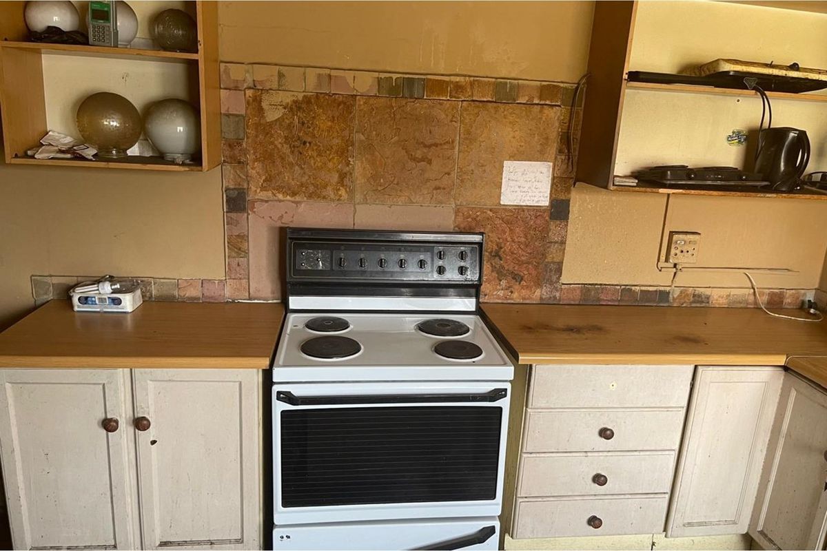 A dated kitchen area featuring a freestanding electric stove, wooden countertops, and built-in cabinetry with a stone-tiled splashback.