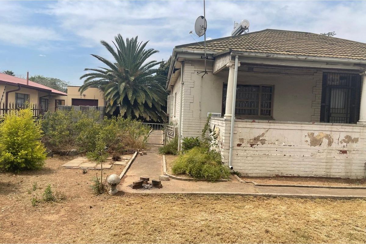 Exterior view of a house featuring a covered porch, brick facade, and a large garden area requiring maintenance and cosmetic restoration.