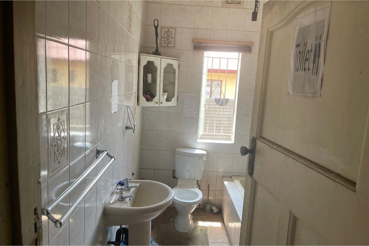 A compact bathroom featuring a pedestal basin, toilet, and built-in bathtub with full-height wall tiling and a security-grilled window.