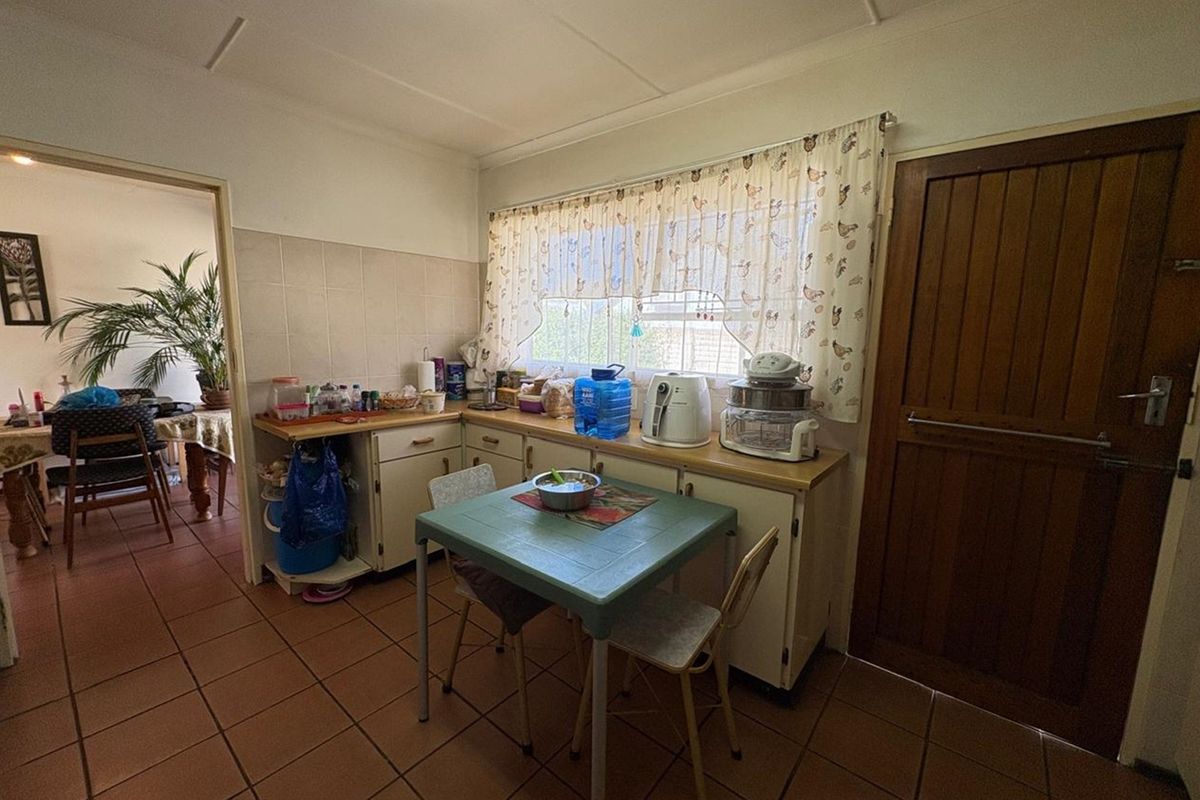 A dated kitchen featuring tiled flooring, built-in cabinetry, and a window overlooking the exterior, with an adjacent view into the dining area.