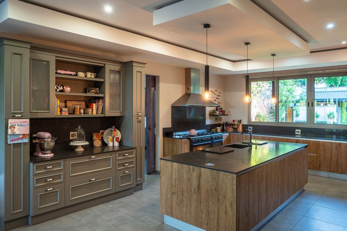 Modern kitchen featuring a large central island, dark stone countertops, custom cabinetry, integrated oven, and a stainless steel extractor fan.
