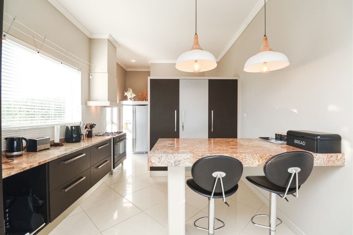 Modern kitchen featuring granite countertops, dark cabinetry, built-in oven, gas hob, extractor fan, and a central breakfast island with pendant lighting.
