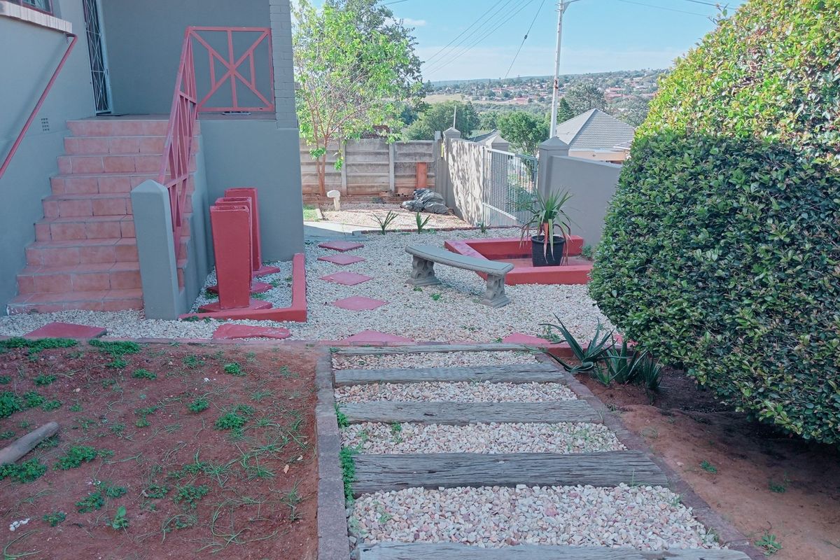 A landscaped rear garden area featuring a gravel pathway, stone steps, and a raised terrace with a view of the surrounding neighborhood.