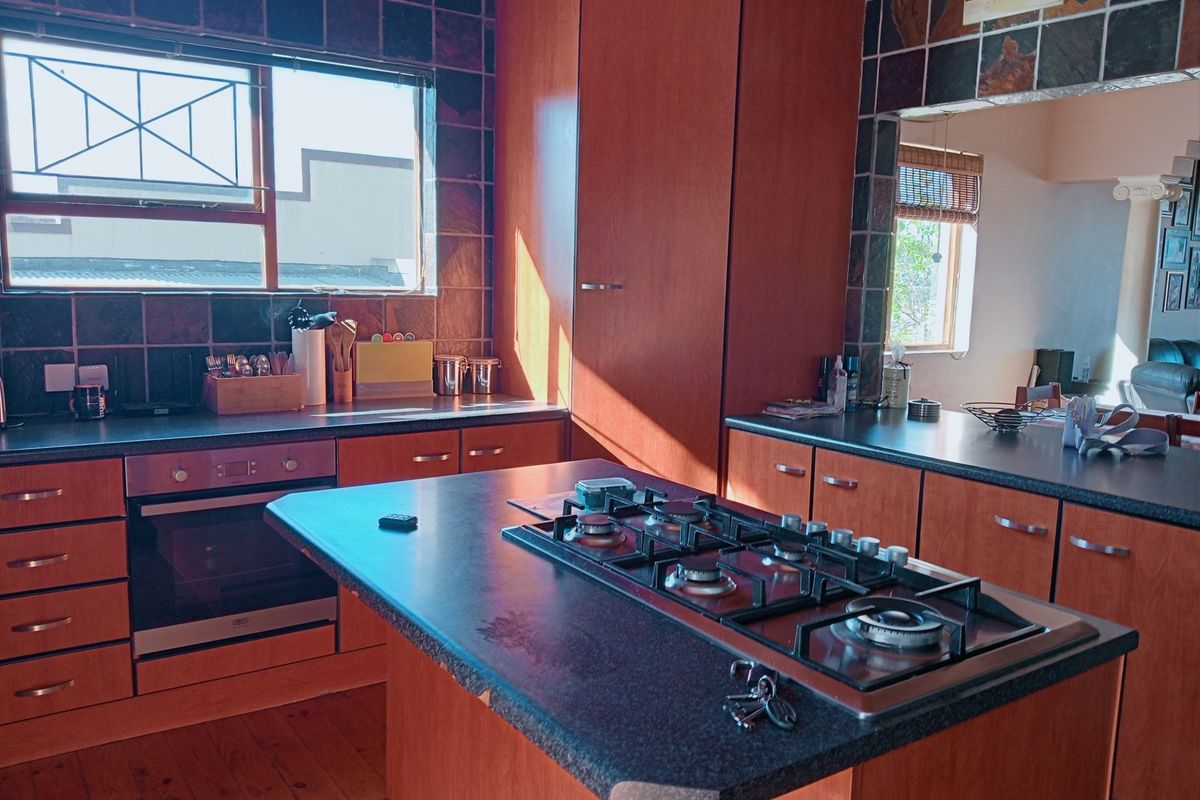 Kitchen featuring wooden cabinetry, dark laminate countertops, a central island with a built-in gas hob, and a wall-mounted oven.