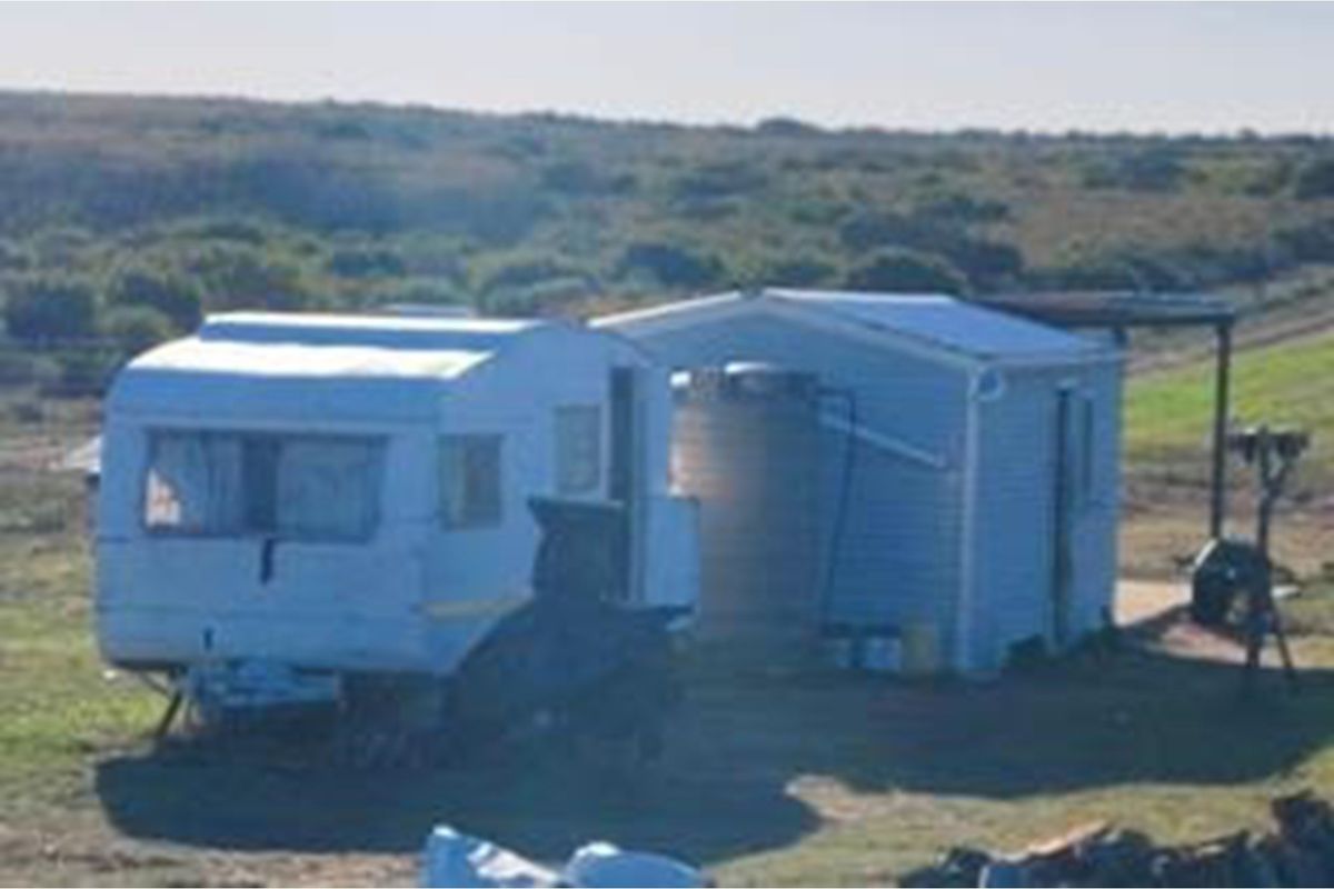 A rustic farm setting featuring a small auxiliary structure with an attached water tank and a caravan on the property grounds.