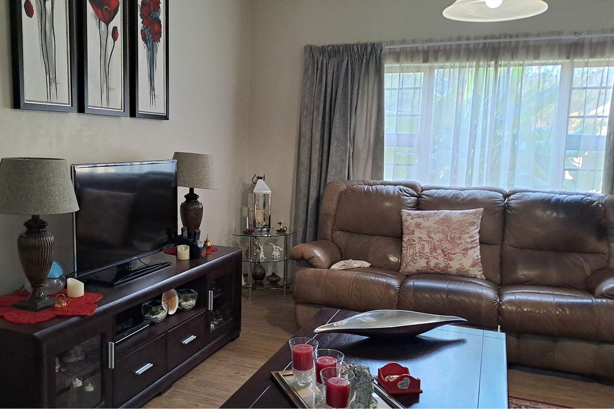 A comfortable living room featuring wood-look flooring, large window with curtains, and neutral wall finishes.