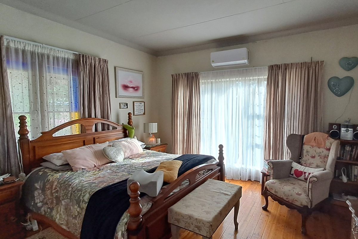 A spacious bedroom featuring polished timber flooring, large windows with curtains, and a wall-mounted air conditioning unit.