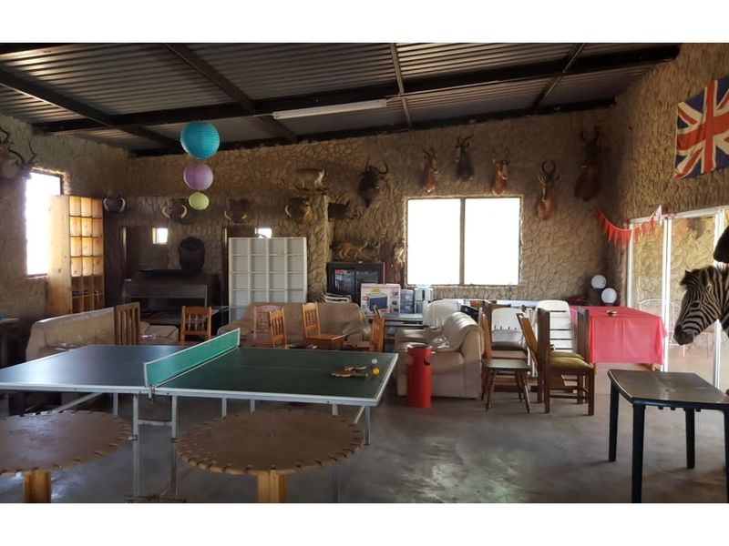 Spacious open-plan entertainment area featuring exposed steel roof trusses, textured stone-clad walls, and large windows, suitable for a versatile recreational space.