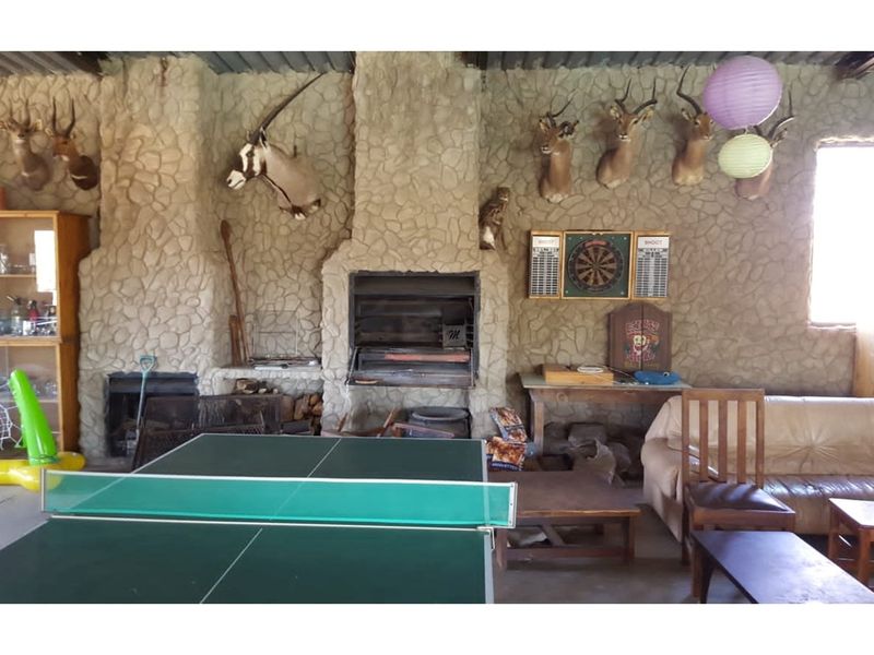 Rustic entertainment area featuring a large stone-clad fireplace, built-in braai, and exposed corrugated metal ceiling, ideal for casual gatherings.