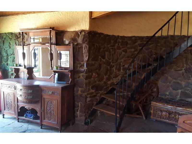 Rustic interior space featuring exposed natural stone walls, a metal staircase, and stone flooring, showcasing a traditional farm-style aesthetic.