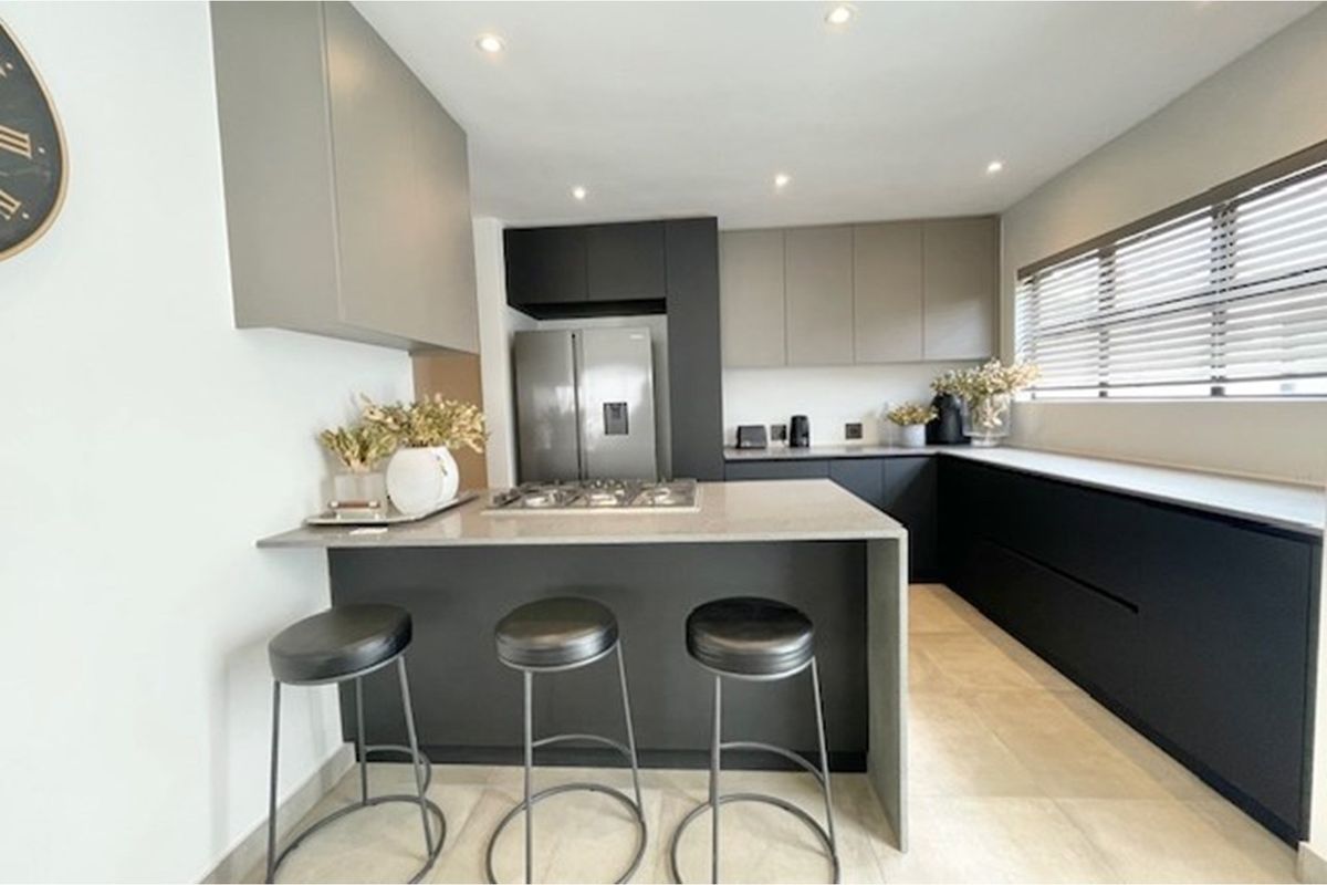 Modern kitchen featuring sleek two-tone cabinetry, stone countertops, a central island with a built-in gas hob, and recessed ceiling lighting.