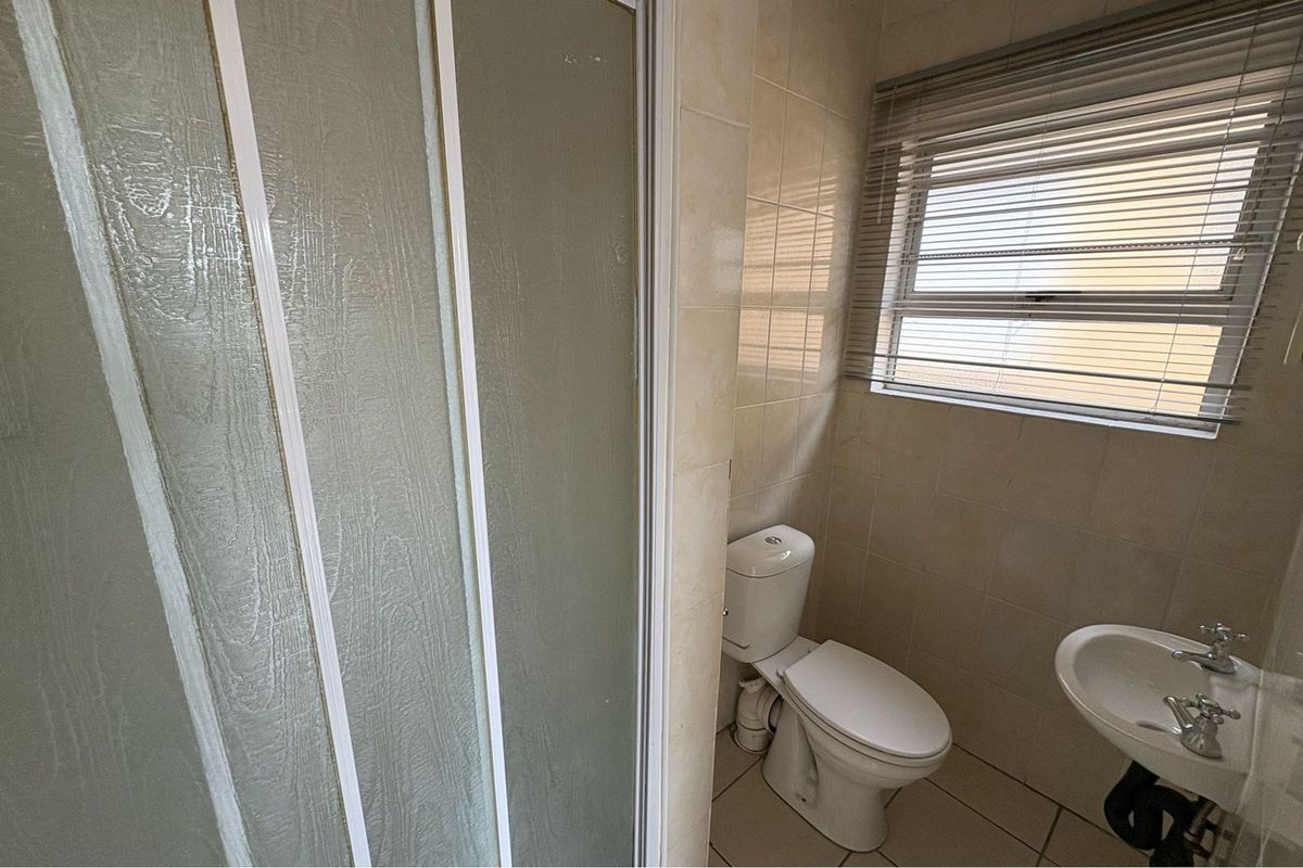 A functional bathroom featuring a shower enclosure, pedestal basin, and toilet, finished with neutral wall and floor tiles.