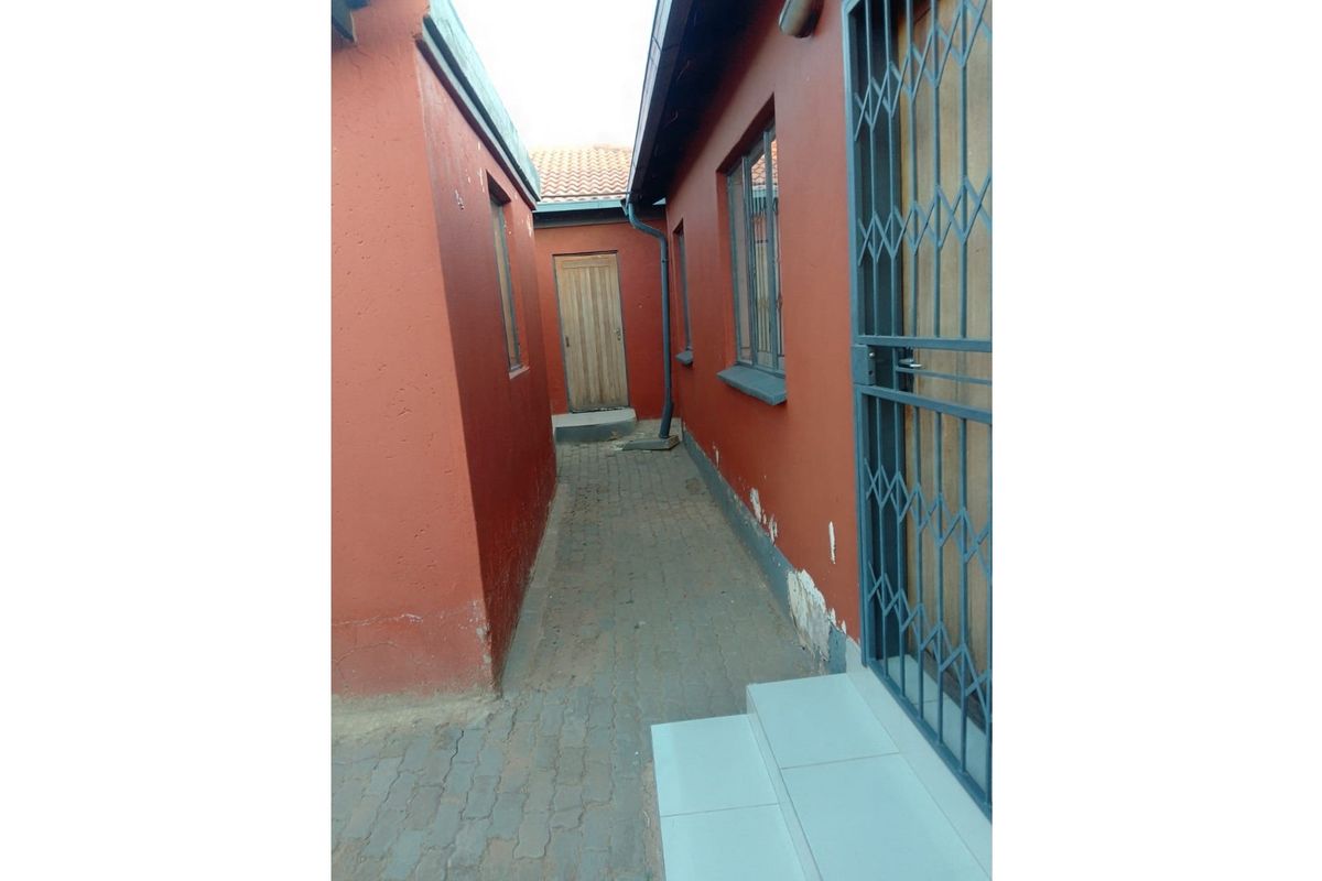 A narrow exterior side passage featuring paved flooring, terracotta-colored walls, and metal security gates, providing access between building sections.