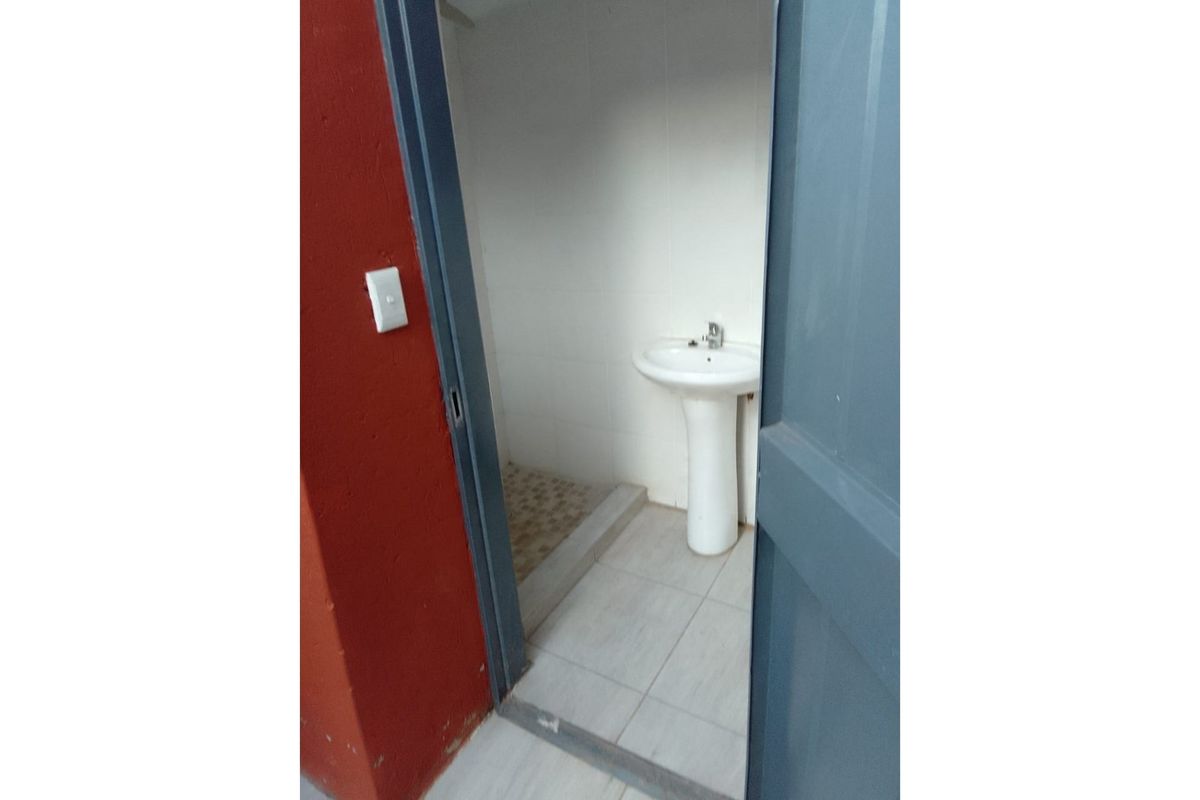 A small, functional bathroom featuring a pedestal basin and tiled flooring, accessed through a doorway.
