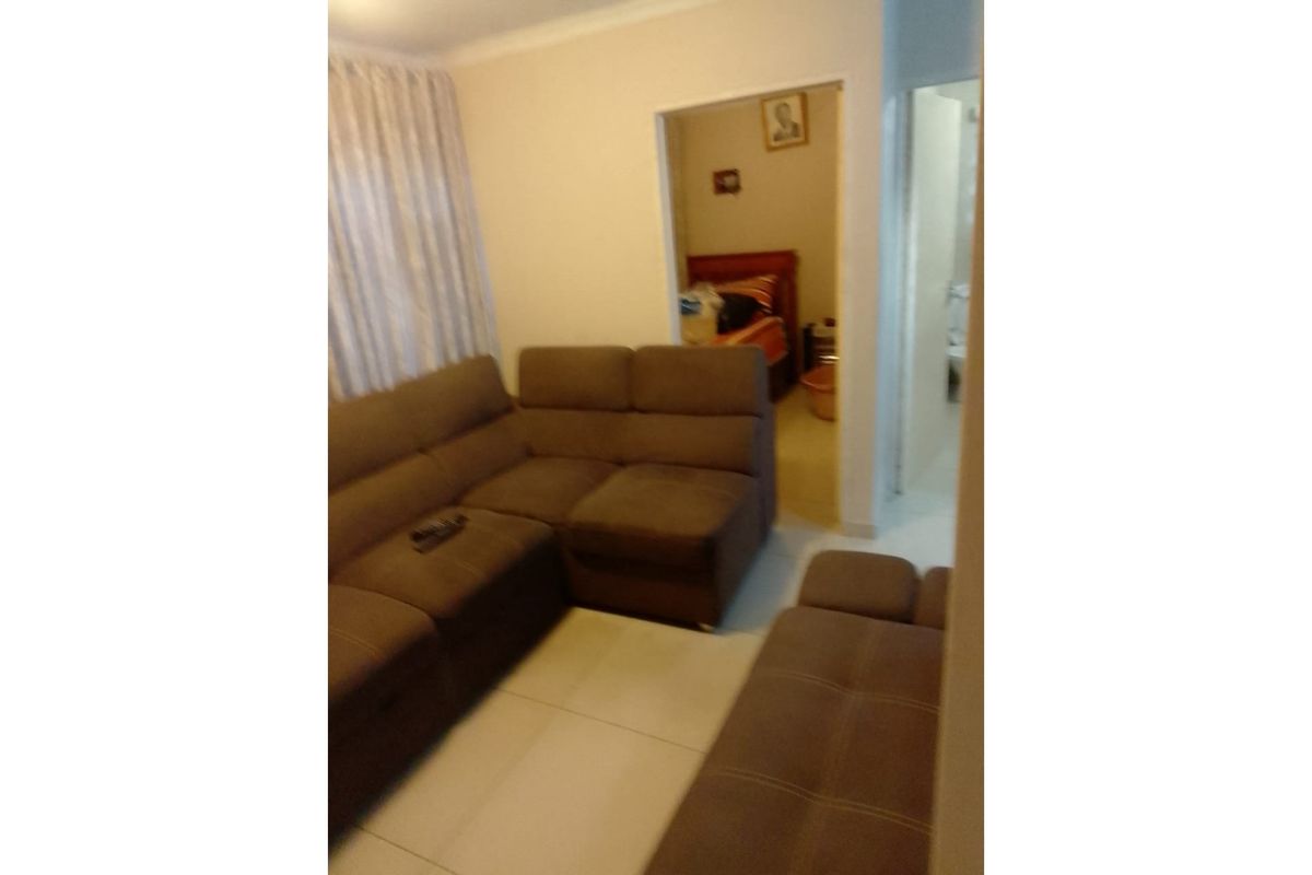 A living room area featuring tiled flooring and a doorway leading to an adjacent bedroom space.