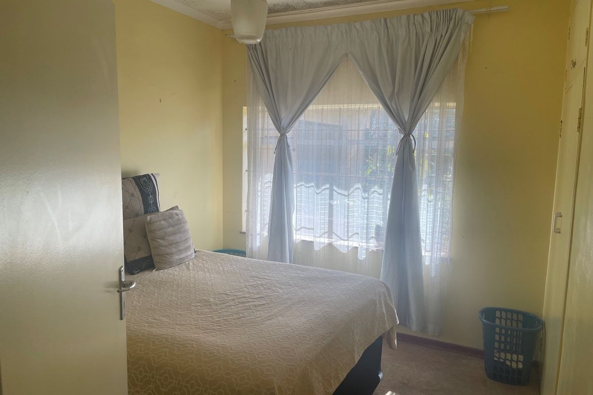 A bedroom featuring built-in cupboards and a window with security bars, requiring cosmetic updates to the ceiling and wall finishes.