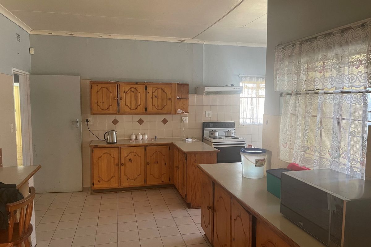 A dated kitchen featuring wooden cabinetry, tiled countertops, and a freestanding stove, offering a functional layout with potential for modernization.