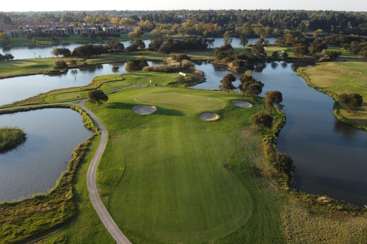 An aerial view of a well-maintained golf course hole featuring a green surrounded by water hazards and sand bunkers.