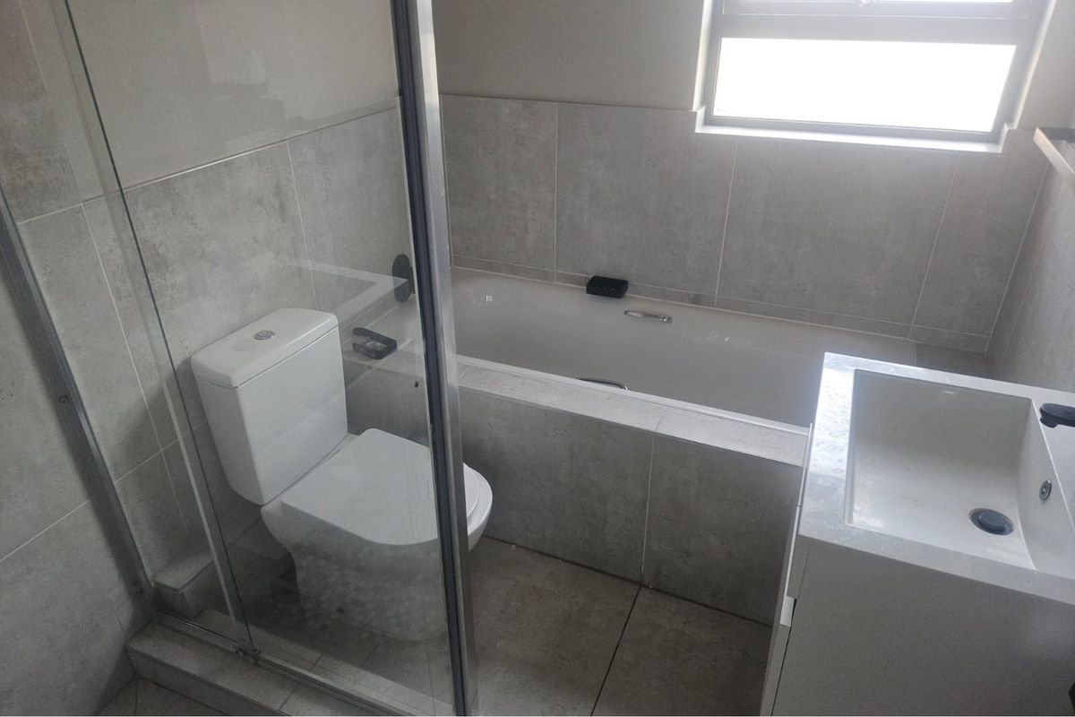 Modern bathroom featuring a built-in bathtub, glass-enclosed shower, wall-mounted toilet, and a sleek vanity basin with neutral grey tiling.