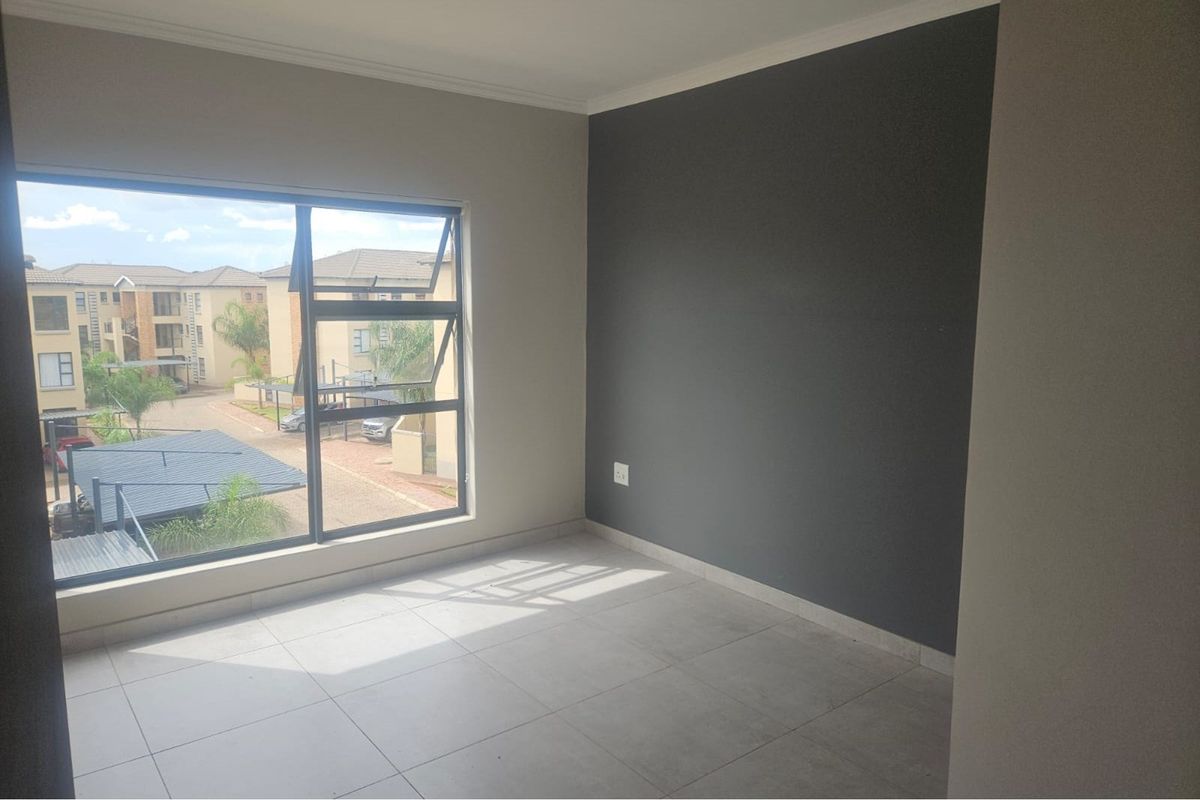 A bright, empty bedroom featuring large aluminium-framed windows, neutral floor tiles, and a dark grey accent wall.