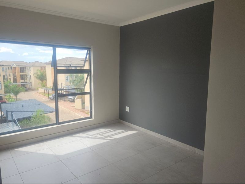 A bright, empty bedroom featuring large aluminium-framed windows, neutral floor tiles, and a dark grey accent wall.
