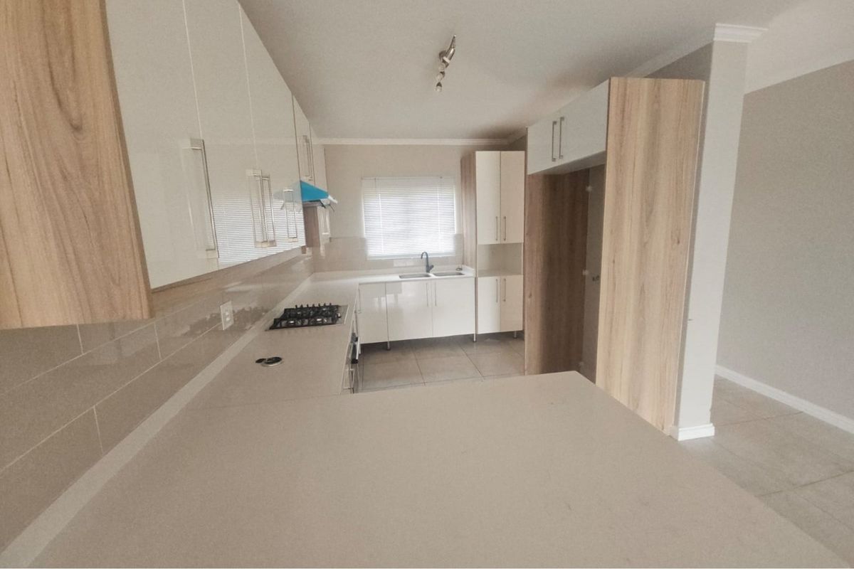 Modern kitchen featuring sleek white cabinetry, wood-grain accents, stone countertops, a built-in gas hob, and a double sink with a window view.