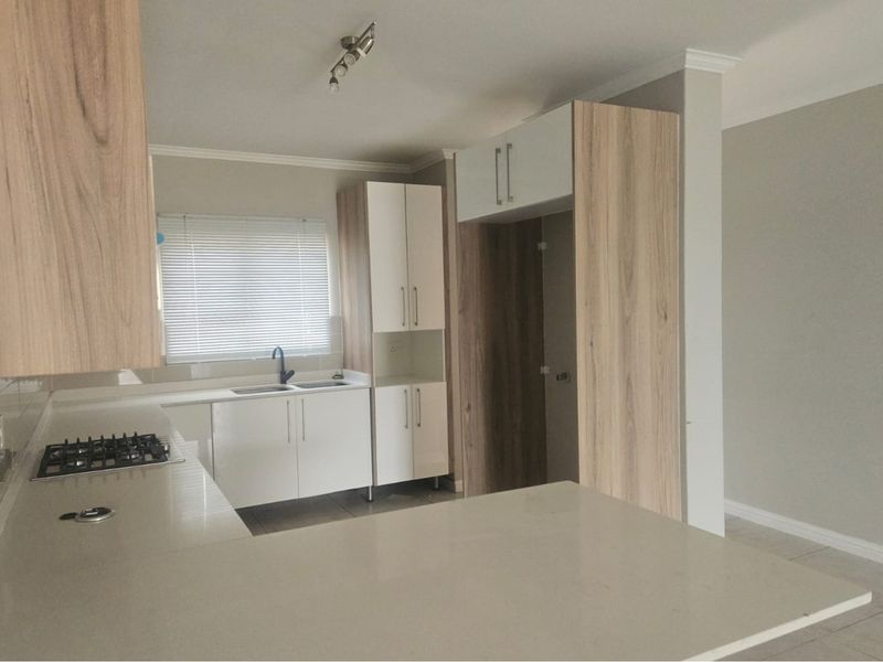 Modern kitchen featuring light wood-grain cabinetry, white stone countertops, a built-in gas hob, and a dedicated space for a refrigerator.