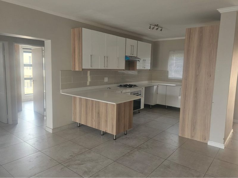 Modern open-plan kitchen featuring white cabinetry, wood-grain accents, stone countertops, built-in gas hob, and tiled flooring throughout.