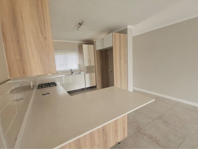 Modern open-plan kitchen featuring light wood-grain cabinetry, stone countertops, a built-in gas hob, and tiled flooring in a bright, neutral space.