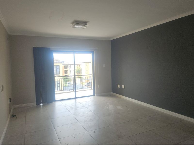 An empty living room featuring large format floor tiles, a dark accent wall, and sliding glass doors leading to a private balcony.