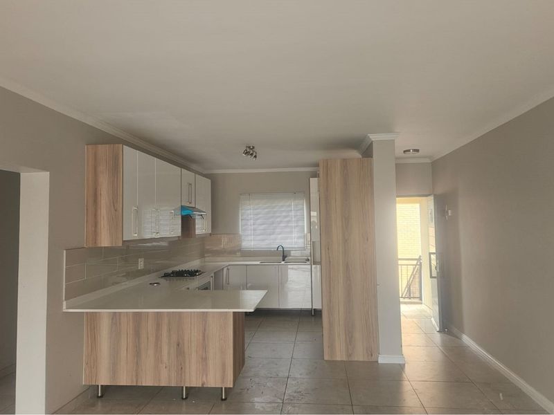 Modern open-plan kitchen featuring light wood-grain cabinetry, white countertops, a built-in gas hob, and tiled flooring, seamlessly connected to the living area.