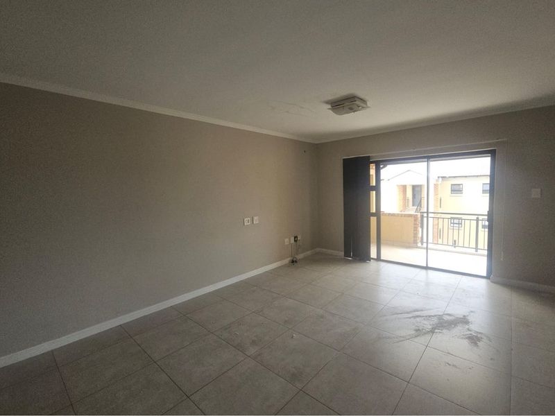 An empty living room featuring neutral tiled flooring, a ceiling-mounted light fixture, and sliding glass doors leading to an outdoor balcony.