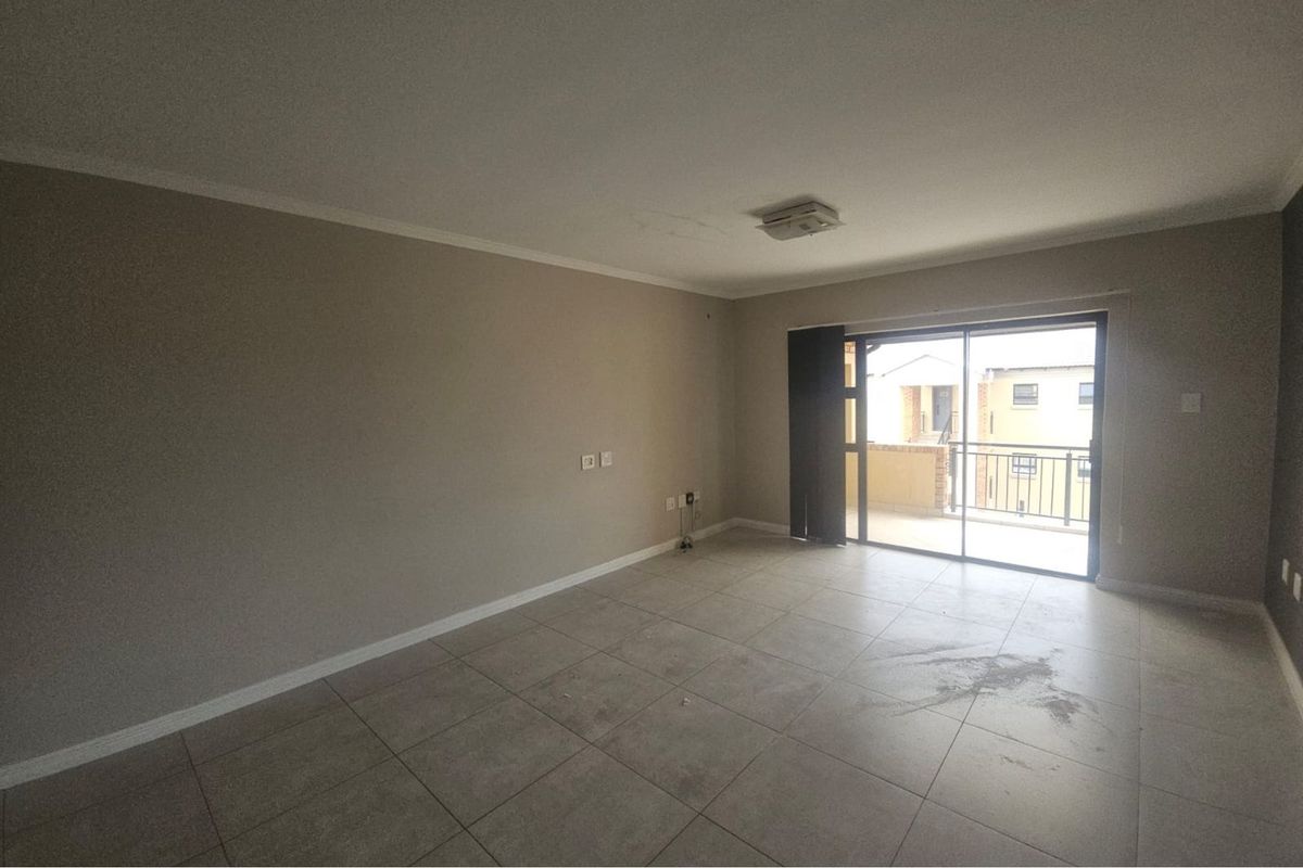 An empty living room featuring neutral tiled flooring, a ceiling-mounted light fixture, and sliding glass doors leading to an outdoor balcony.
