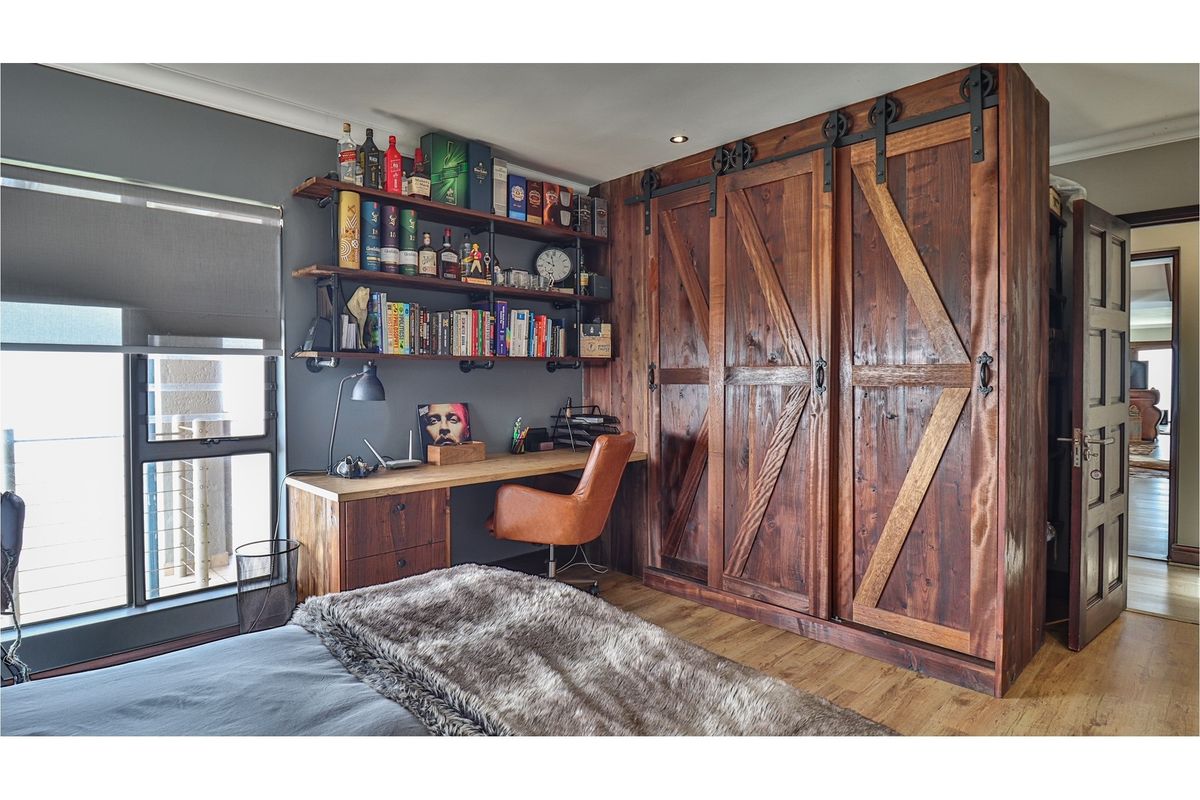 A well-appointed bedroom featuring custom rustic timber barn-style sliding wardrobe doors and a built-in wooden desk with industrial-style shelving.