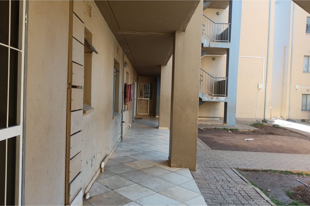 Exterior view of an apartment building walkway featuring tiled flooring, concrete pillars, and access to an external metal staircase.
