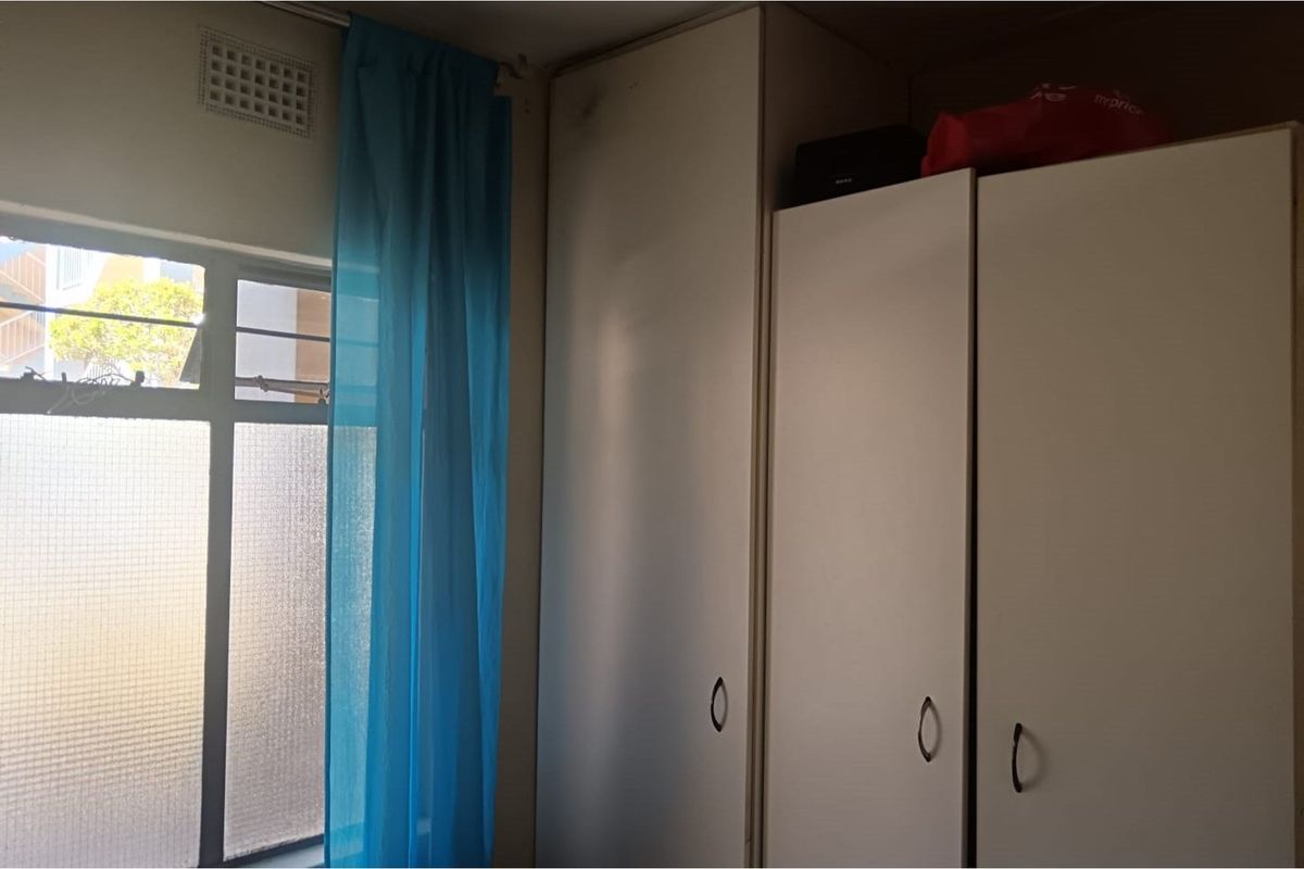 A bedroom featuring built-in cupboards and a window with natural light, providing functional storage space.