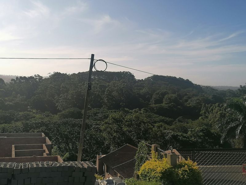 Elevated view overlooking a lush green landscape with surrounding residential development and utility infrastructure.