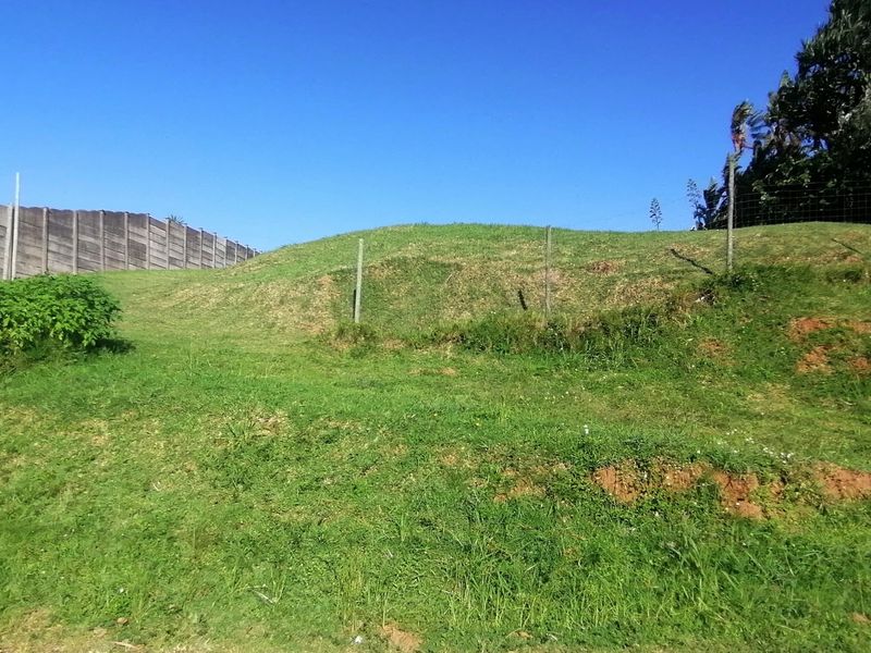 A sloped residential plot featuring a precast concrete boundary wall and wire mesh fencing, offering a clear view of the undeveloped land.
