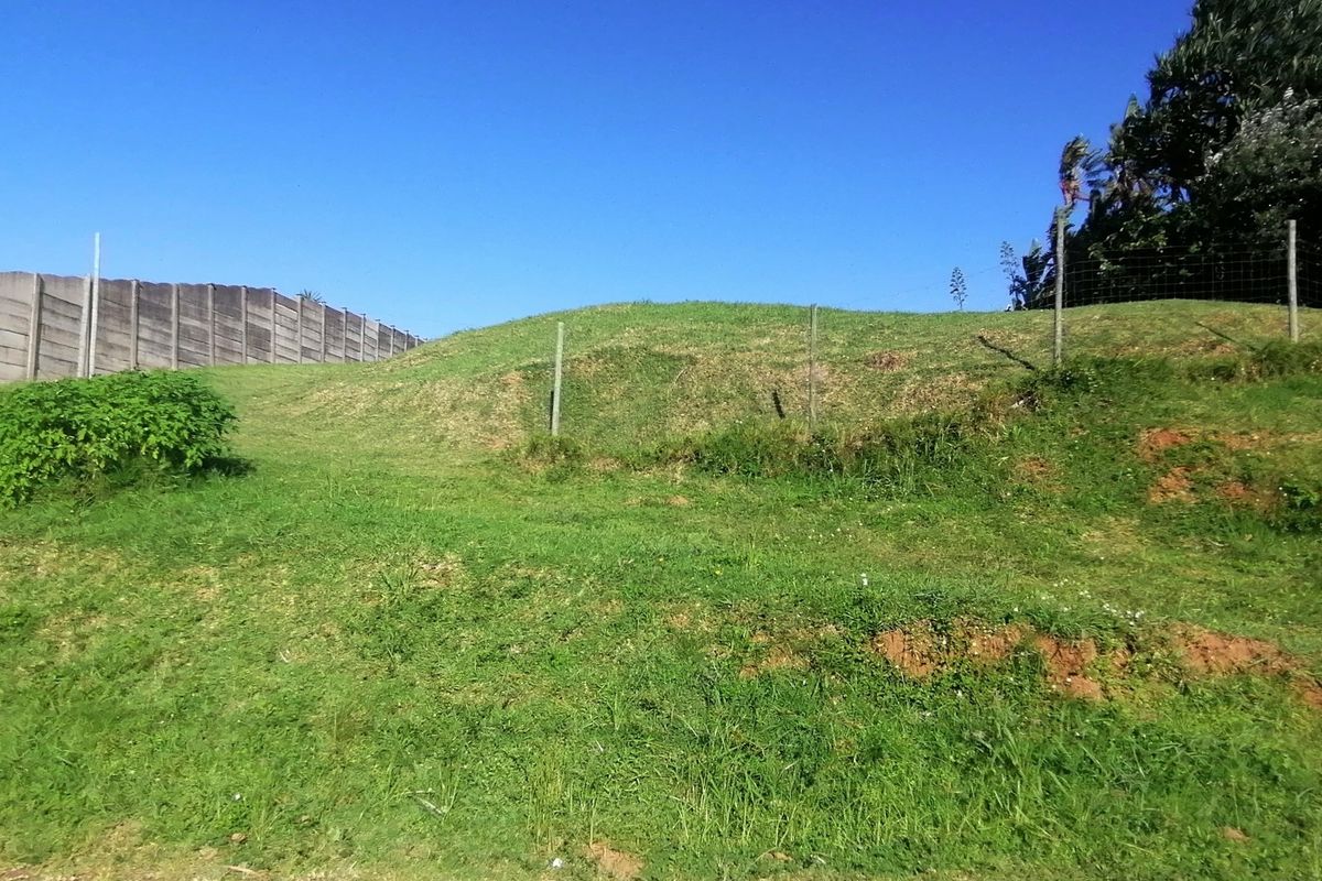 A sloped residential plot featuring a precast concrete boundary wall and wire mesh fencing, offering a clear view of the undeveloped land.
