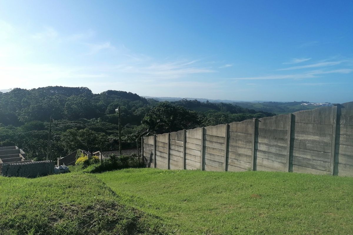 A view of a sloped residential plot featuring a precast concrete boundary wall and surrounding natural landscape.