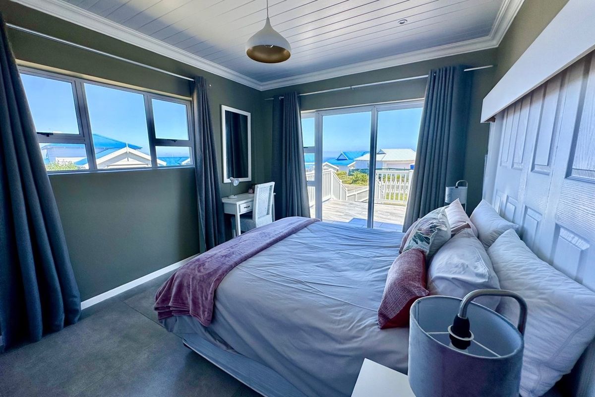 A well-maintained bedroom featuring a tongue-and-groove ceiling, tiled flooring, and sliding glass doors that open onto a deck with coastal views.