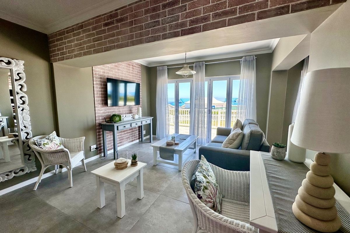 A bright living room featuring exposed brick accent walls, large glass sliding doors leading to a balcony, and neutral tiled flooring.