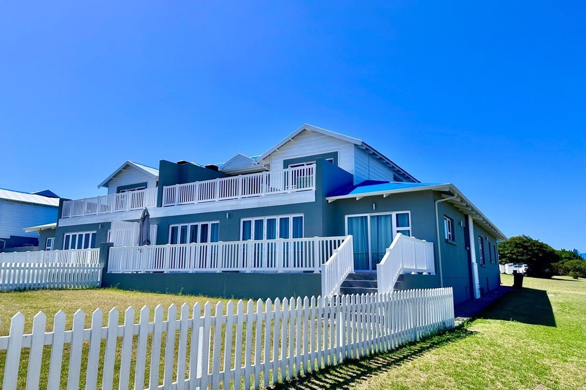 A well-maintained multi-level residential property featuring expansive balconies, white picket fencing, and a blue roof set against a clear sky.