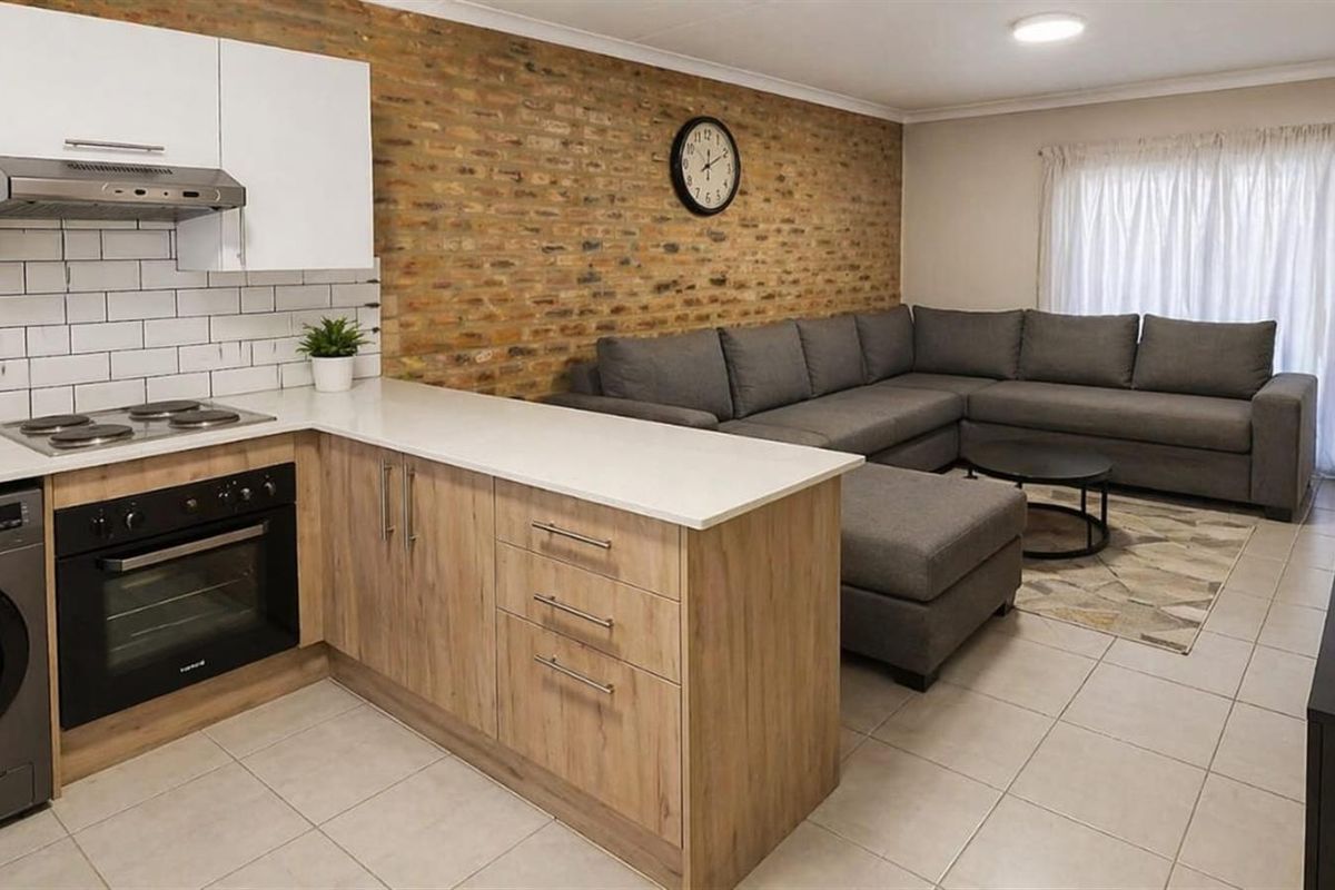 Open-plan living area featuring a modern kitchen with light wood cabinetry, white countertops, subway tile backsplash, and integrated oven and hob.