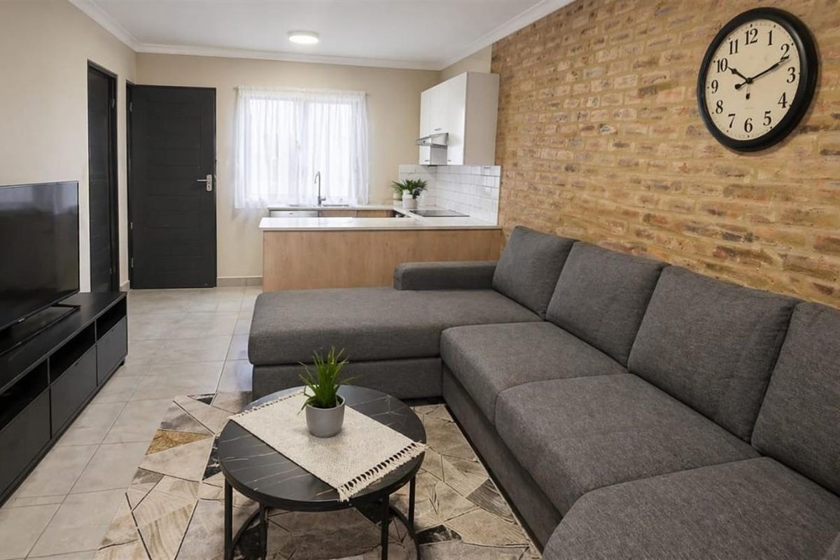Open-plan living area featuring a modern kitchen with light wood cabinetry and a distinctive exposed brick feature wall.
