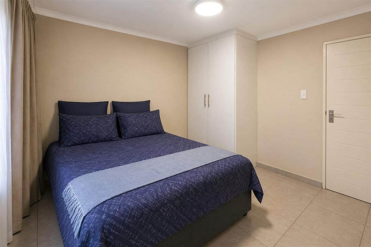 A well-maintained bedroom featuring neutral wall tones, tiled flooring, and built-in wardrobe storage.