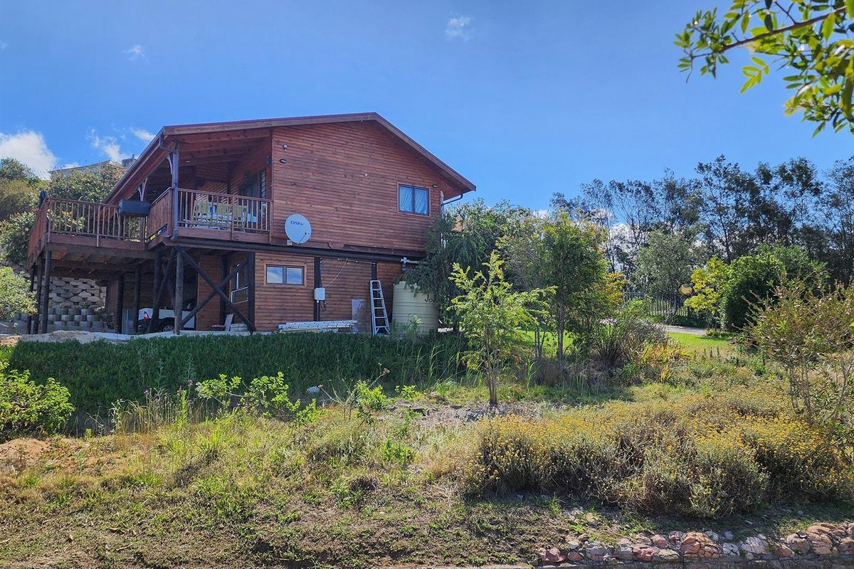 A two-story timber-clad residential dwelling featuring an elevated wooden deck, set within a landscaped garden plot.