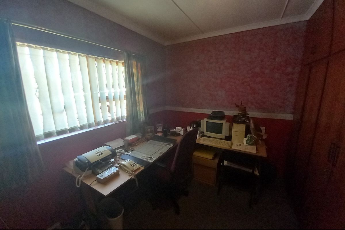 A bedroom featuring built-in wooden cupboards and vertical window blinds, currently utilized as a home office space.