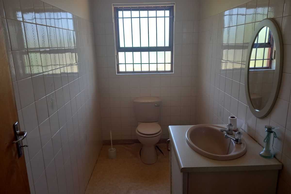 A compact bathroom featuring a standard toilet, a built-in vanity with a basin, and full-height wall tiling with security bars on the window.