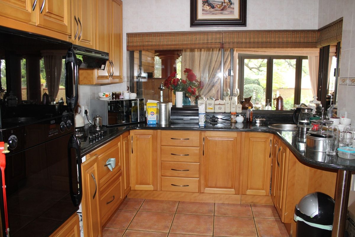 A functional kitchen featuring wooden cabinetry, granite countertops, built-in oven, extractor fan, and ceramic tile flooring with a view to the garden.